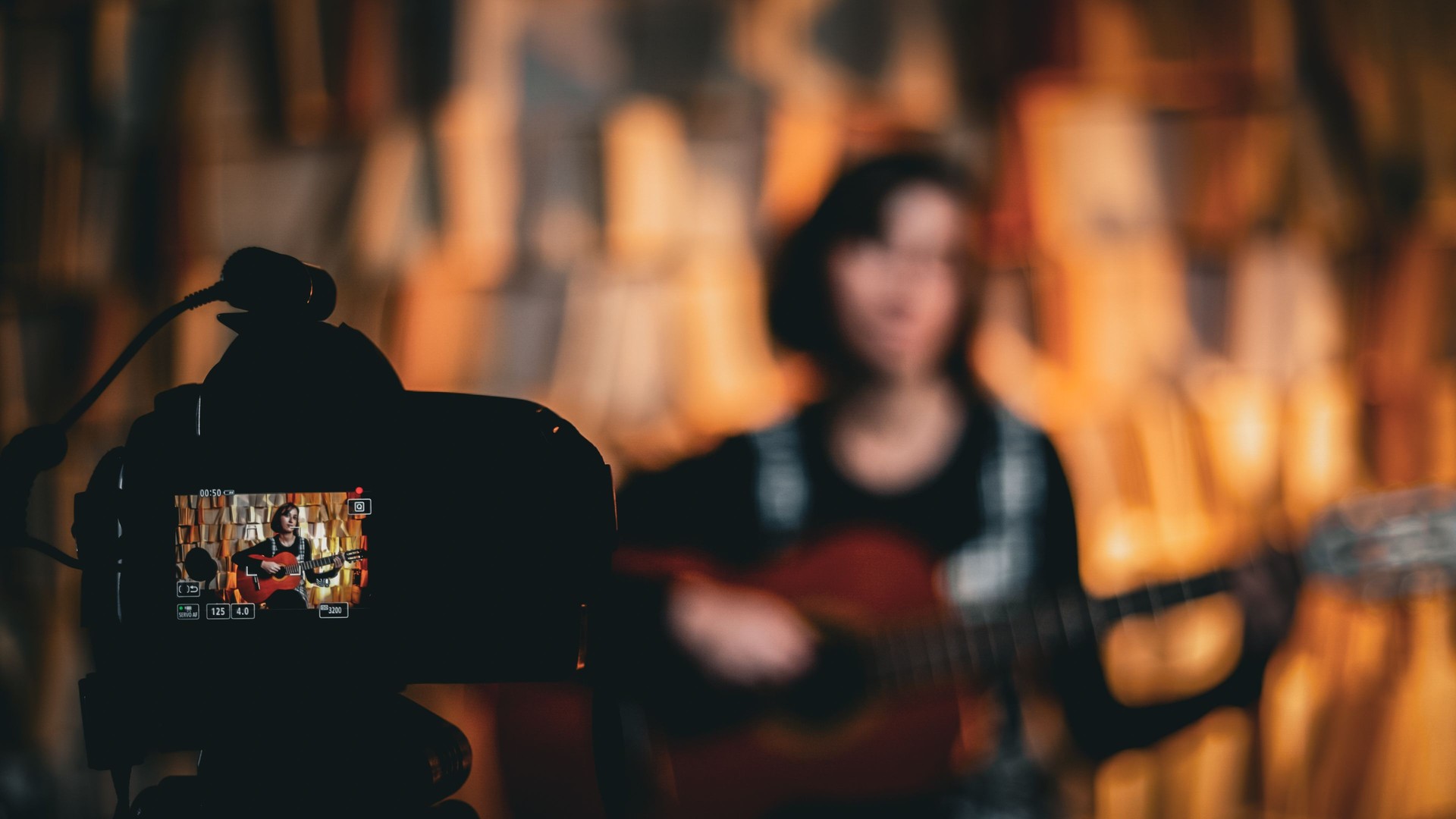 Woman playing guitar filming herself with camera, Young woman playing guitar looking at camera shot, training vlog training video course for social media in studio, live musician, woman playing guitar is broadcasting live